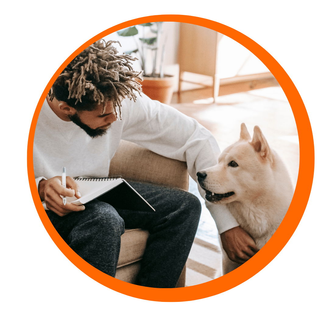 Man petting his dog while he's writing in a notebook